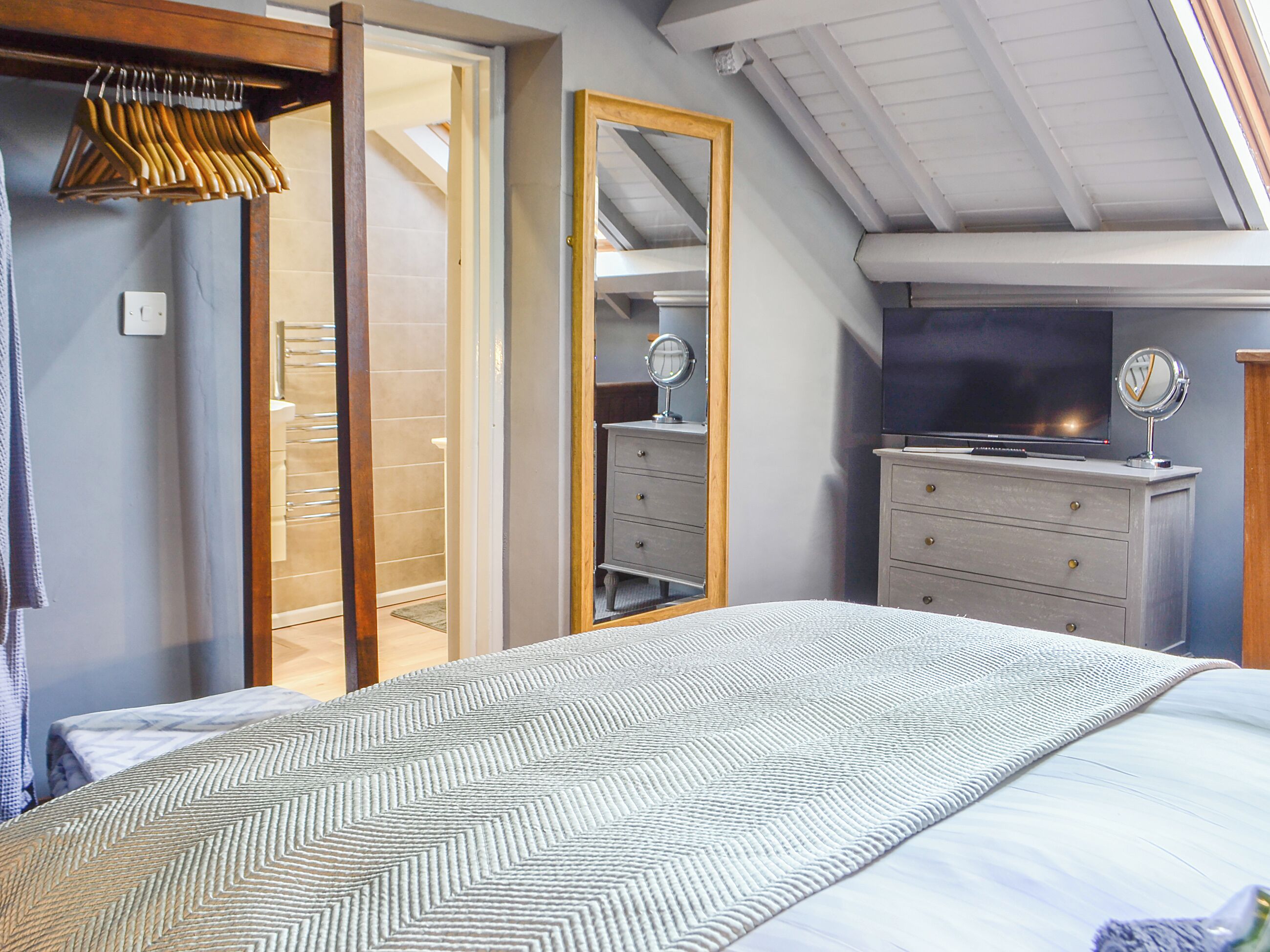 Een slaapkamer met een bed, een dressoir, een spiegel en een televisie.