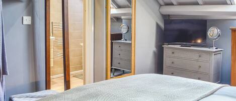 Een slaapkamer met een bed, een dressoir, een spiegel en een televisie.