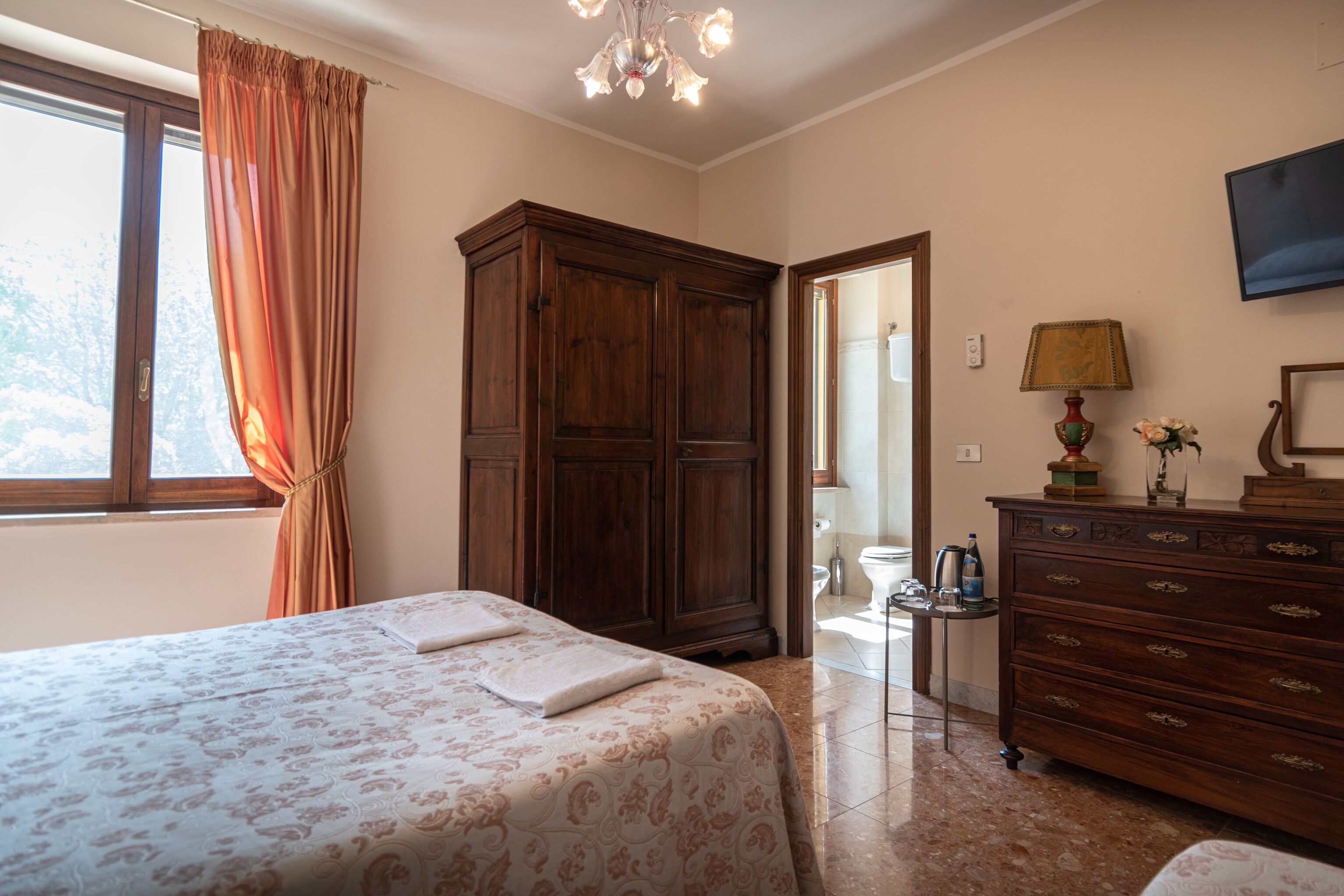 A bedroom with a bed, wooden wardrobe, and a desk with a lamp.