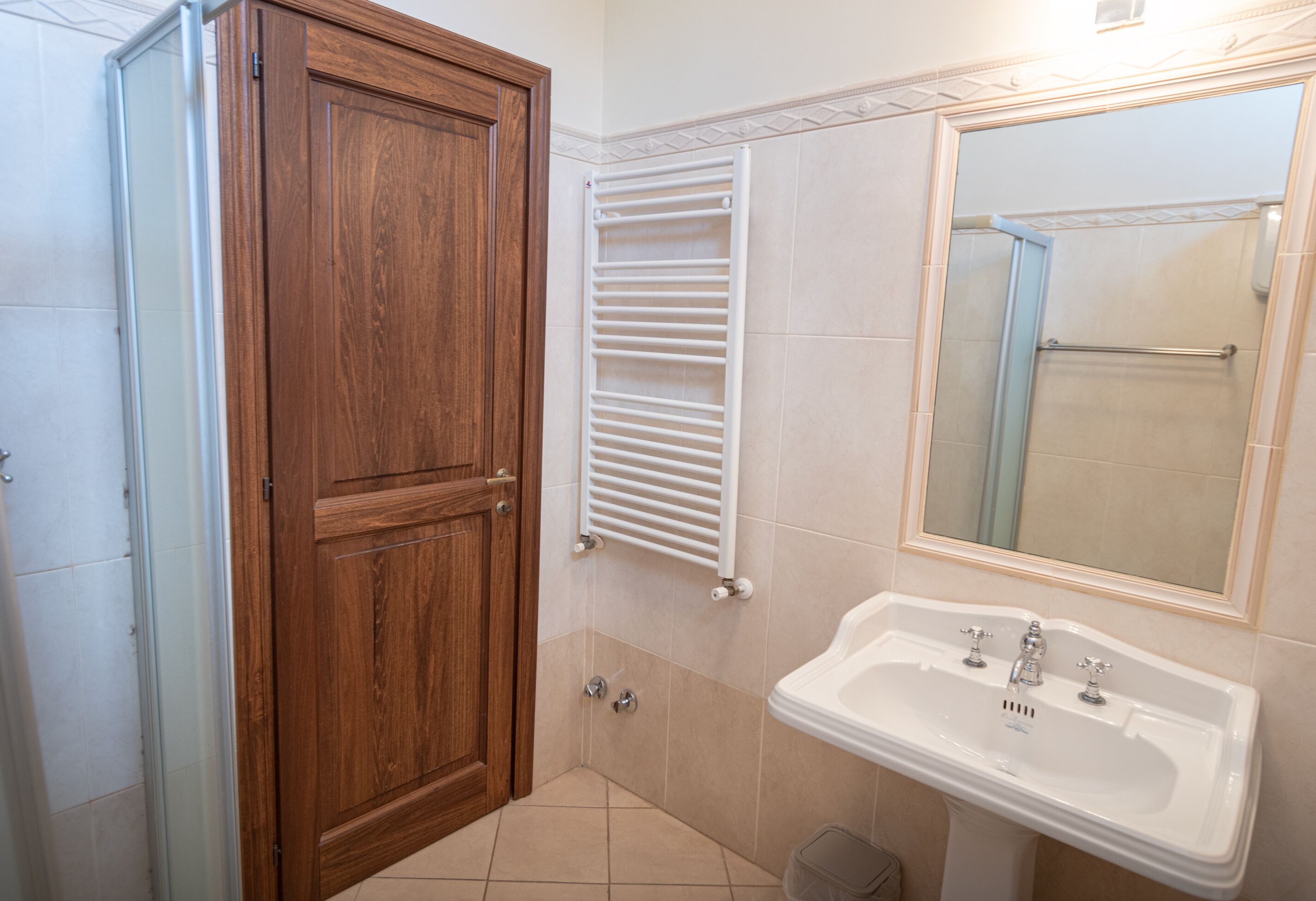 A bathroom with a wooden door, a white towel rack, a sink, and a mirror.