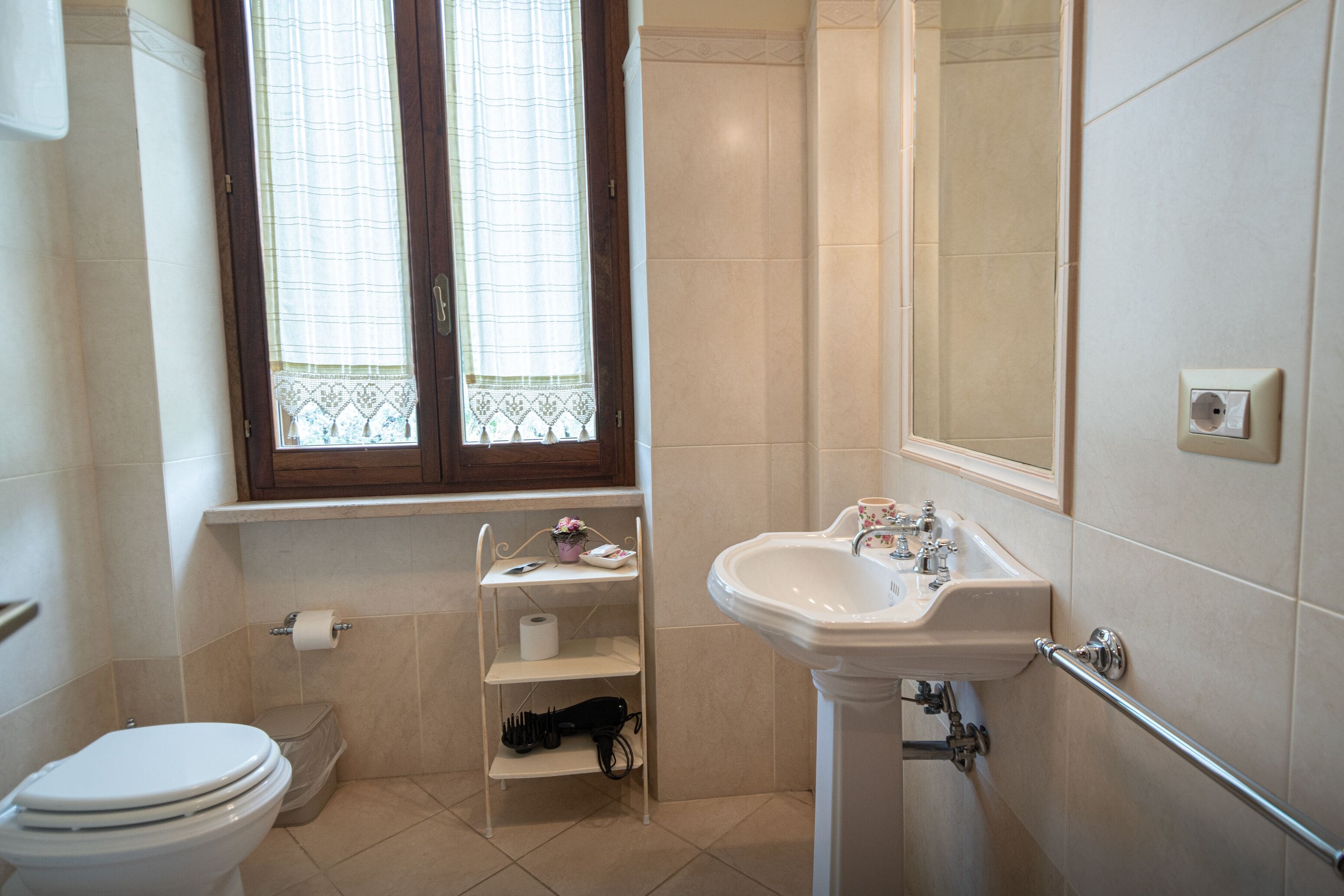 A bathroom with a toilet, a sink, and a window with a curtain.