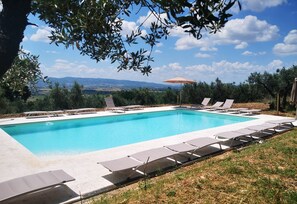 A rectangular swimming pool with lounge chairs and an umbrella, surrounded by greenery and a view of distant mountains. - Villa Val d'Olivi (Assisi)