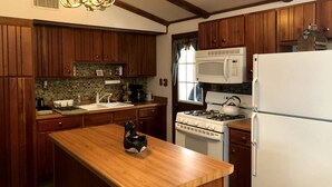 A kitchen with wooden cabinets, a white stove, a microwave, and a refrigerator. - Spectacular waterfront setting, comfy cabin (Hazelhurst)