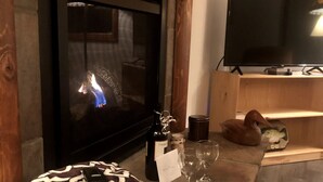 A cozy living room with a fireplace, a television, and a patterned cushion on a stone bench. - Spectacular waterfront setting, comfy cabin (Hazelhurst)