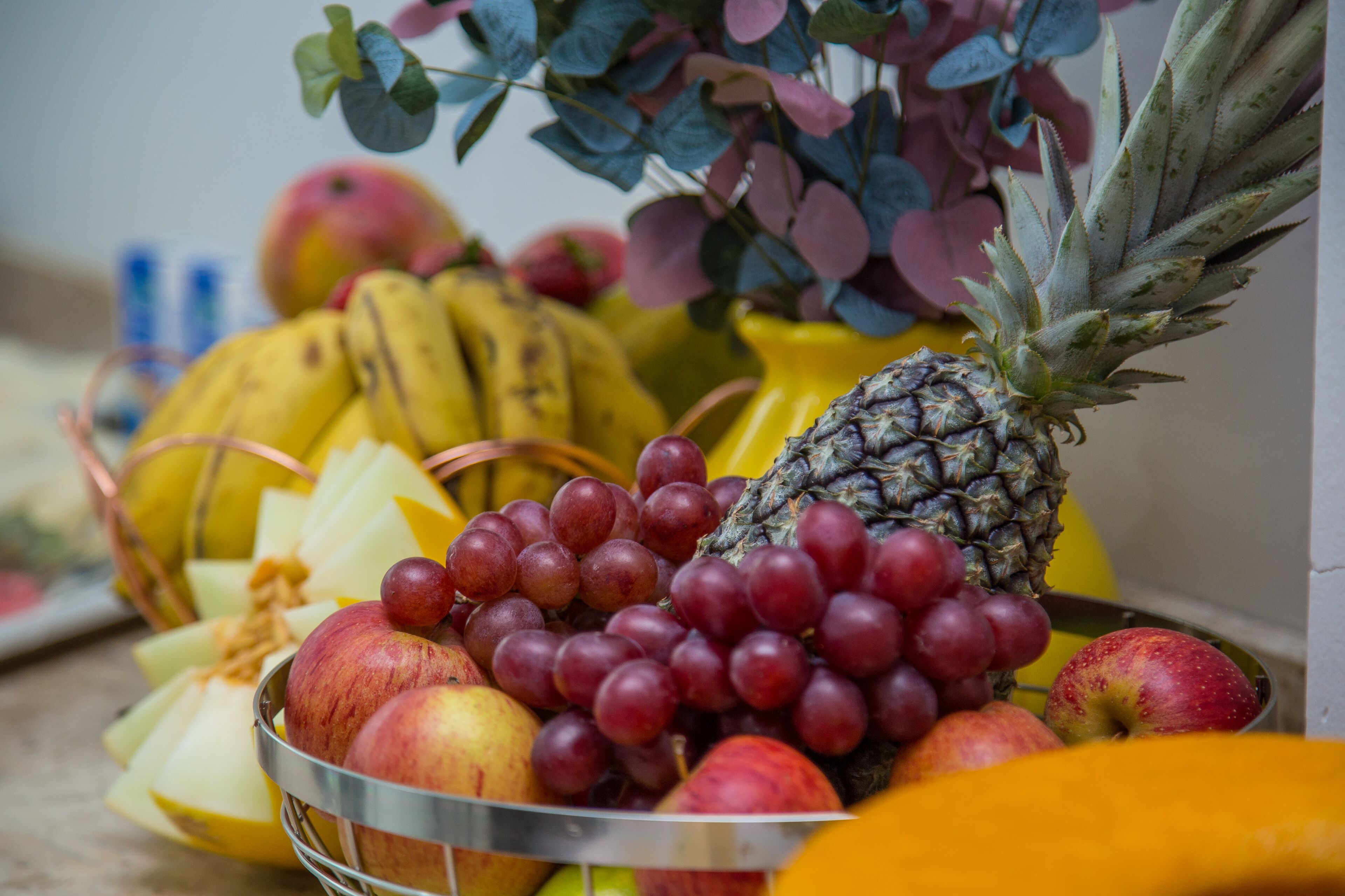 A fruit bowl containing apples, grapes, bananas, and pineapple.