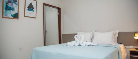 A hotel room with a bed, a nightstand, a lamp, an air conditioner, and two framed pictures on the wall.