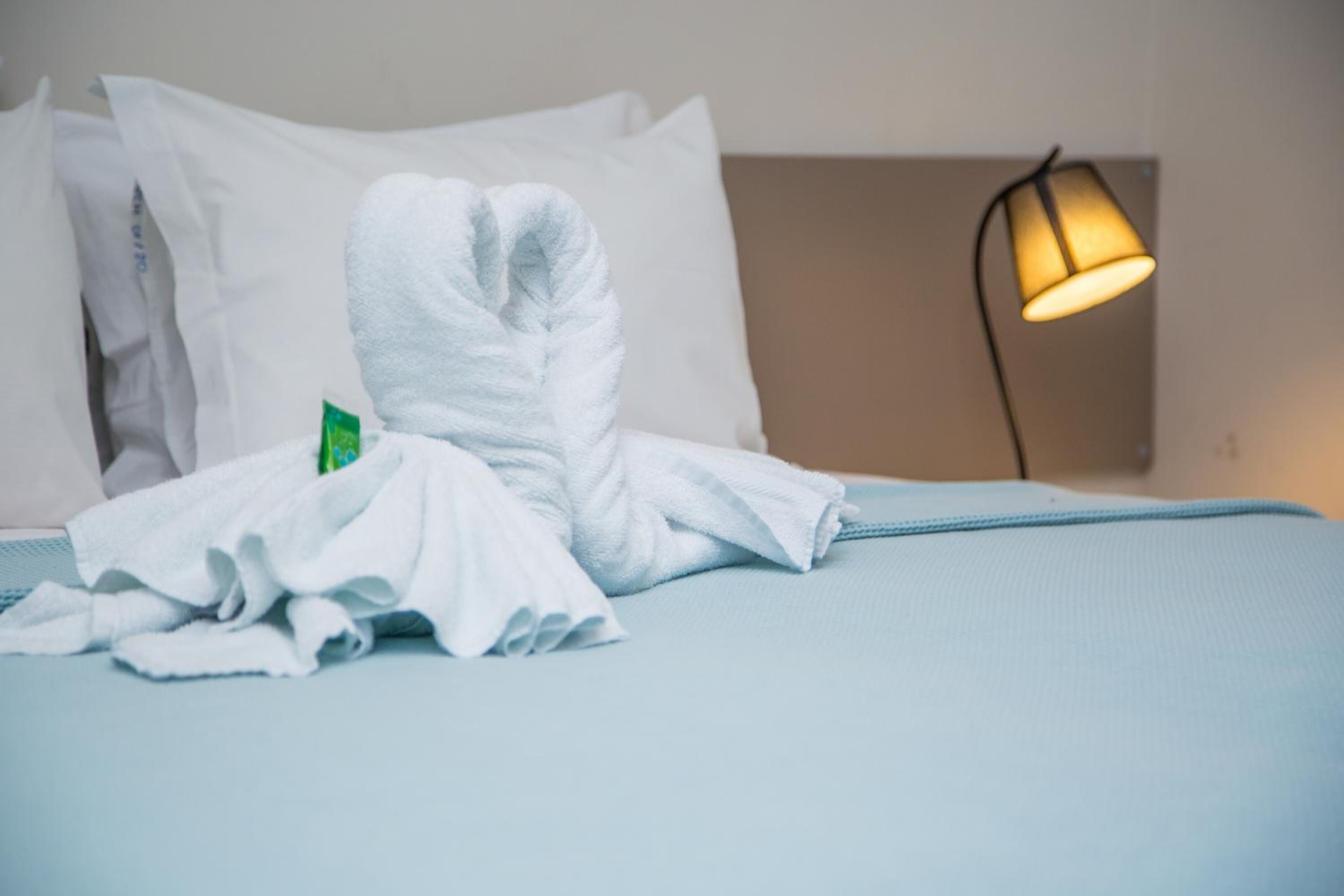 A neatly made bed with white towels, a green tissue, and a lamp on the side.