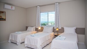 Una habitación de hotel con dos camas individuales, un ventanal con cortinas, un aire acondicionado instalado en la pared y un cuadro colgado.