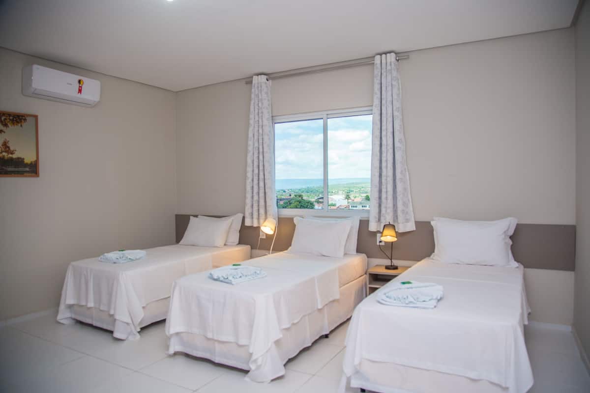 Una habitación de hotel con dos camas individuales, un ventanal con cortinas, un aire acondicionado instalado en la pared y un cuadro colgado.