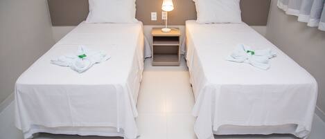 Una habitación de hotel con dos camas individuales, una mesita de noche con lámpara y un par de toallas sobre cada cama.