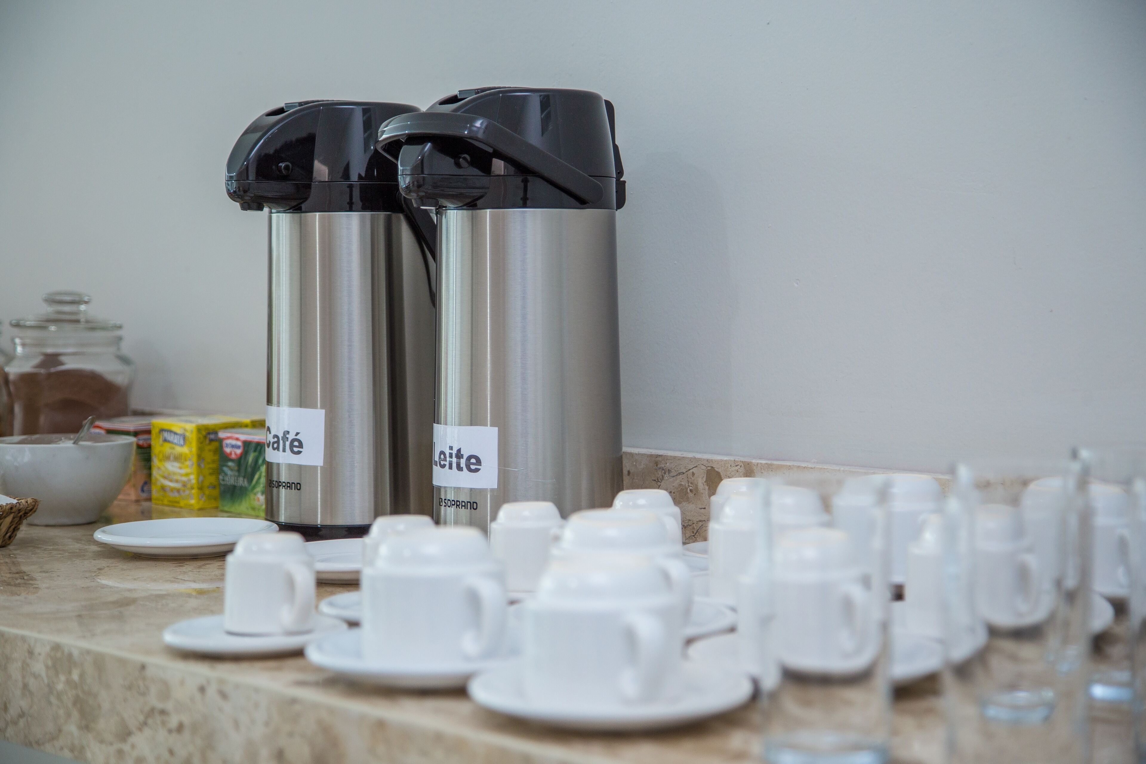 A breakfast setup with two stainless steel coffee dispensers labeled "Café Leite," a bowl, and a carton of milk.