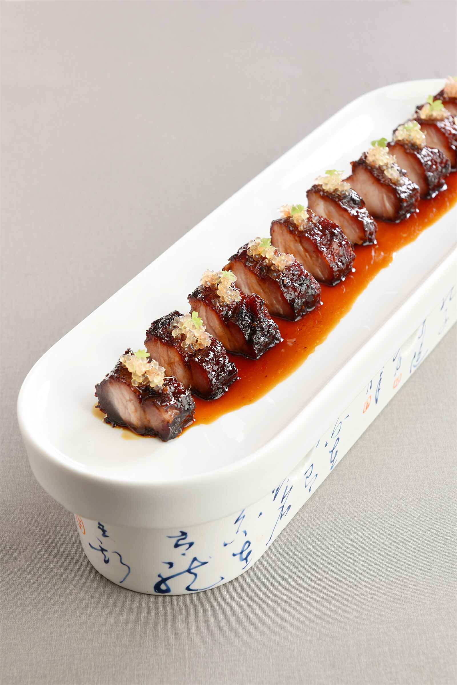 A white rectangular dish with a decorative border, containing sliced meat garnished with green and white toppings, and a dark sauce.