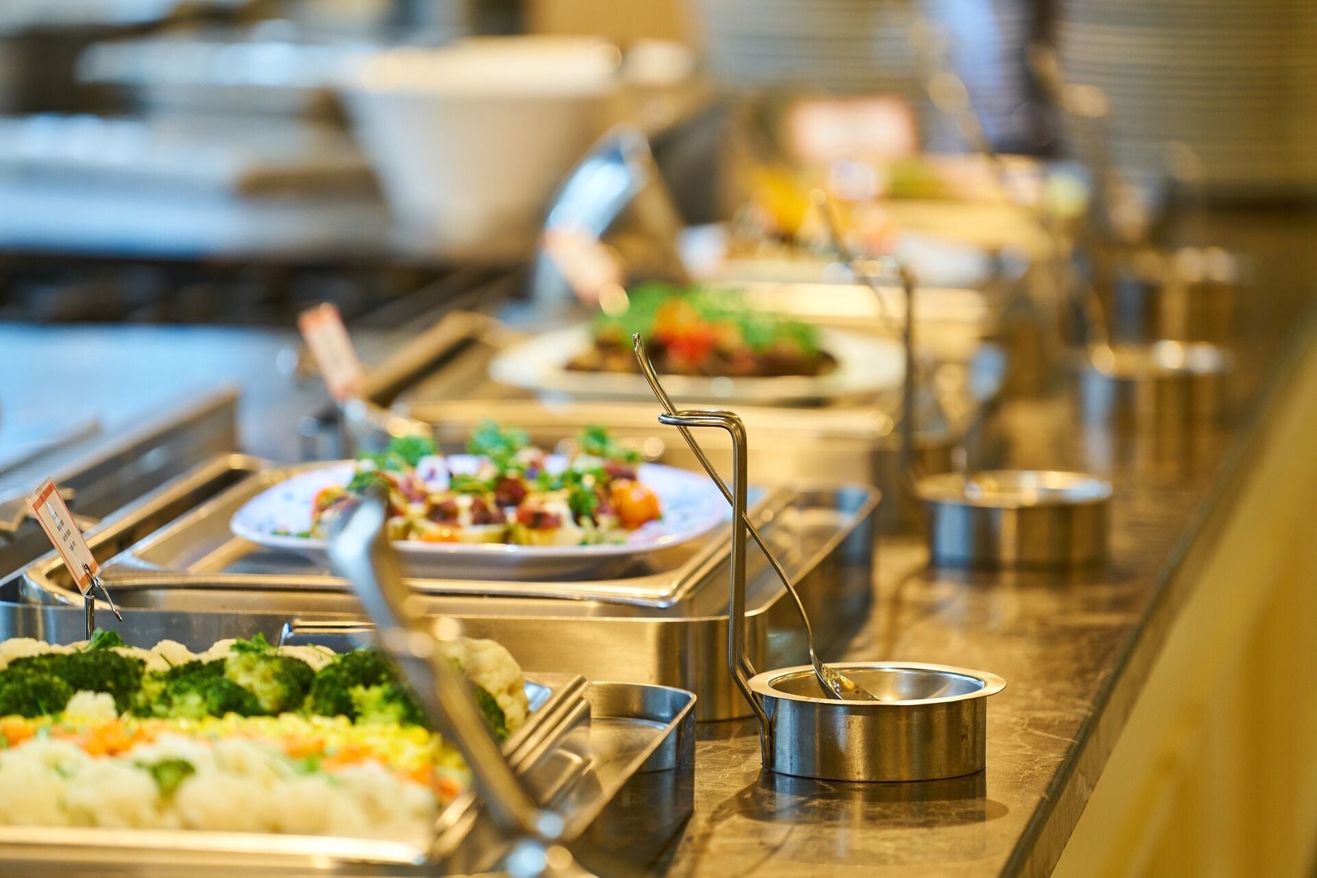 A buffet with various dishes, including vegetables and salads, arranged on a stainless steel counter.