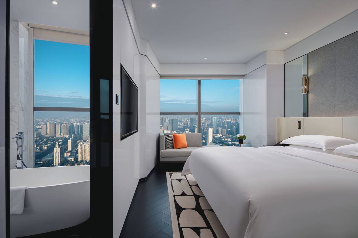 Une chambre d’hôtel moderne avec un grand lit, un canapé, une télévision et une vue sur la ville.