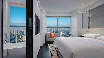 Una habitación de hotel moderna con una cama grande, un sofá, un televisor y vistas a la ciudad.