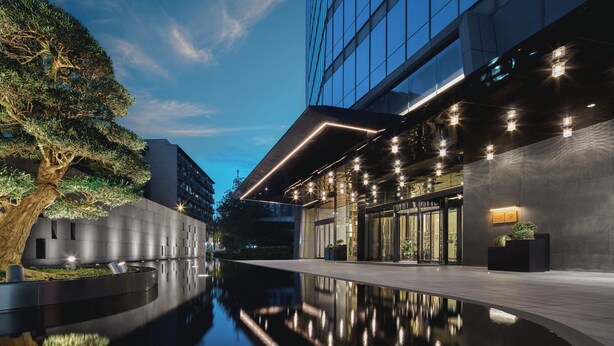 Un edificio moderno con una piscina reflectante, ventanas amplias y un árbol.