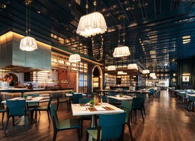 A spacious restaurant with high ceilings, modern pendant lighting, and a mix of seating arrangements.
