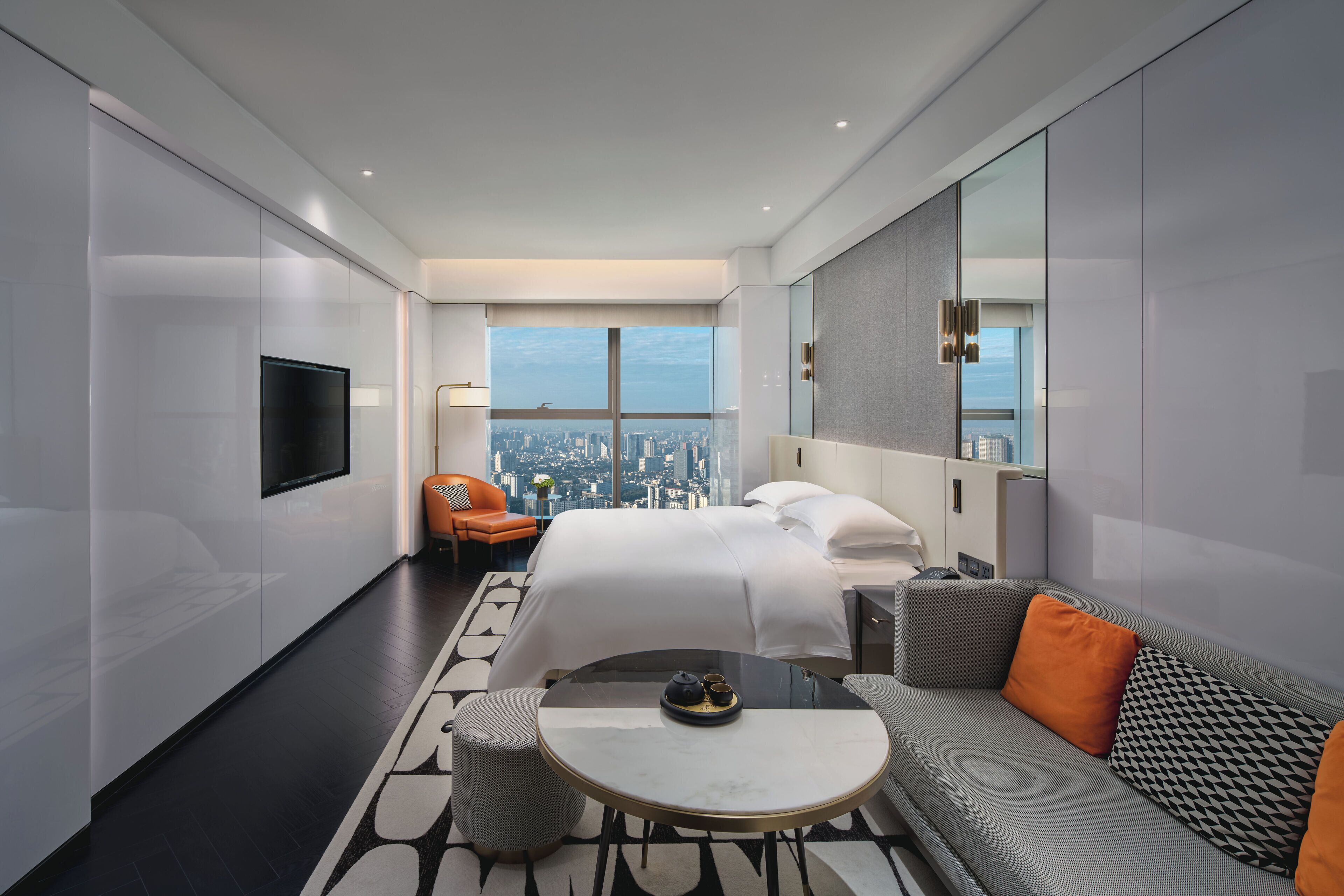 Una habitación de hotel moderna con una cama grande, un sofá, una mesita redonda y vistas a la ciudad.