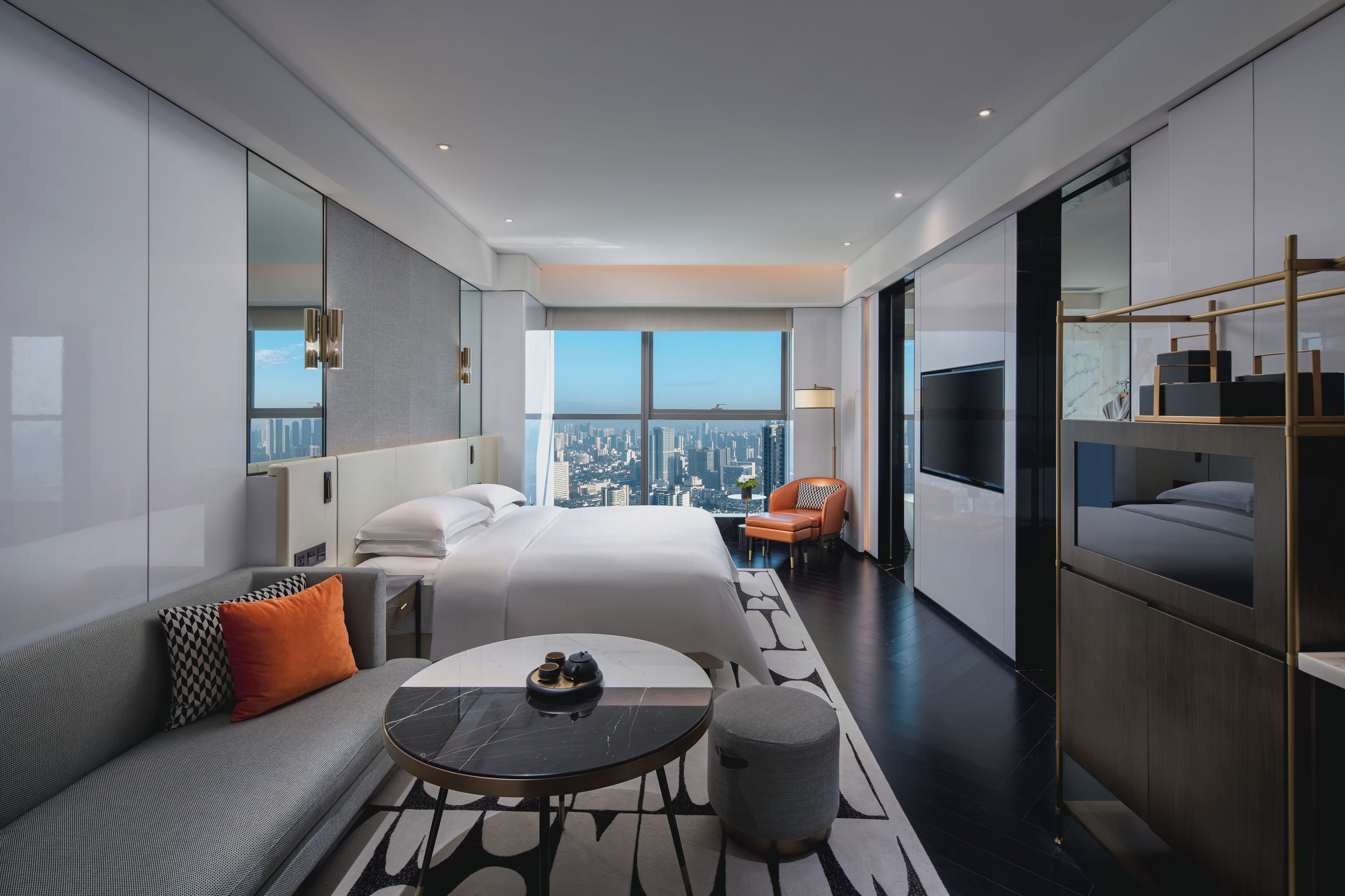 A modern hotel room with a large bed, a sofa, a small table, and a TV.