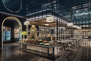 A modern restaurant interior with a central buffet, wooden flooring, and a glass ceiling.