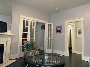 A living room with a fireplace, a patterned armchair, a glass-top coffee table, and a door leading to another room. - A Remote Worker's Paradise (Savannah)