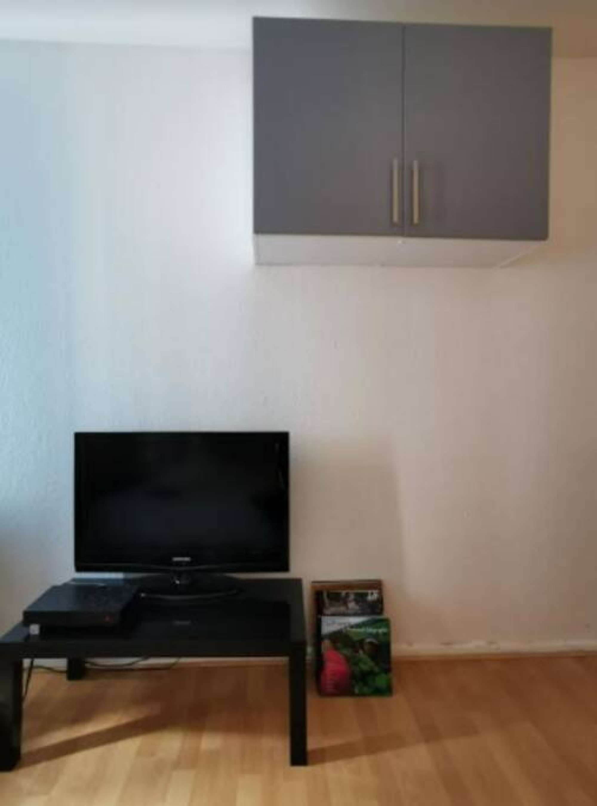 Una habitación con un televisor sobre un soporte, un armario gris arriba y una caja en el suelo.