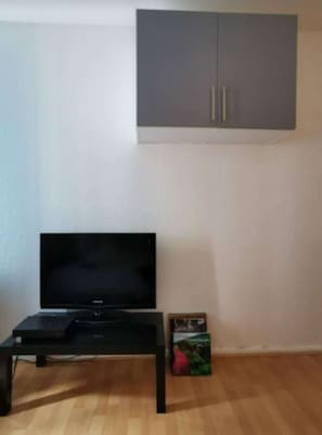 A room with a television on a stand, a grey cabinet above, and a box on the floor.