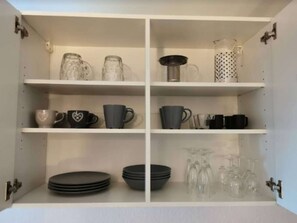 Een witte kast met vier planken, elk gevuld met verschillende keukengerei.