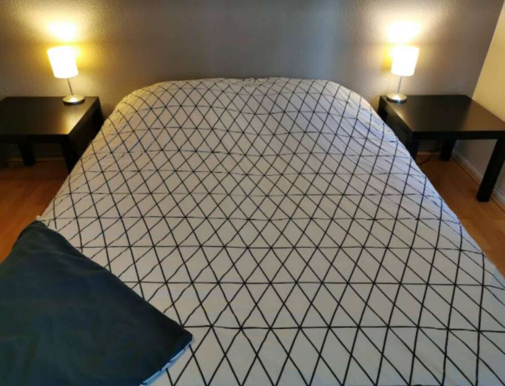 Un lit recouvert d’une couvre-lit à motifs géométriques, deux tables de chevet avec des lampes et un plancher en bois.