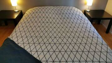 Un lit recouvert d’une couvre-lit à motifs géométriques, deux tables de chevet avec des lampes et un plancher en bois.