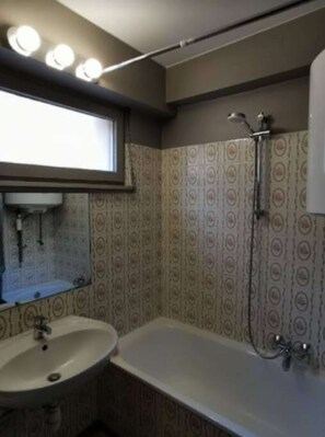 Een badkamer met een wastafel, spiegel, douche en behang met een patroon.