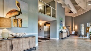 A spacious lobby with a high ceiling, a wooden reception desk, a painting of a pelican, and an elevator. - Oceanfront and beachfront with absolutely unbelievable views! (Destin)