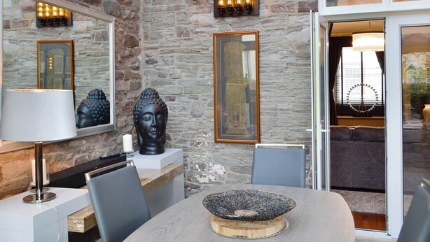 Un comedor moderno con una pared de piedra, una estatua de Buda y un amplio ventanal con vistas a una noria.