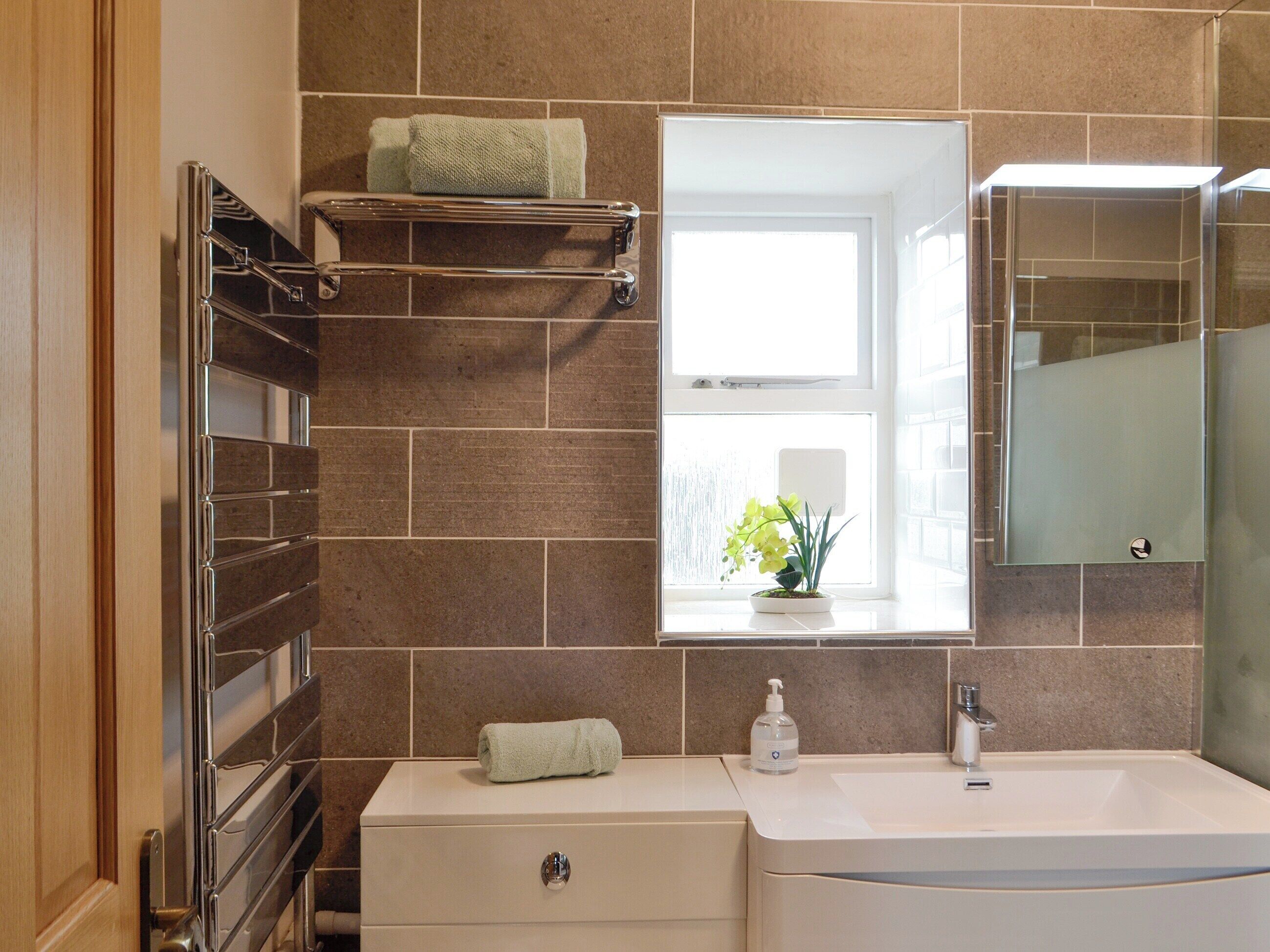 A bathroom with a white sink, a mirror, a towel rack, and a window with a view of flowers.