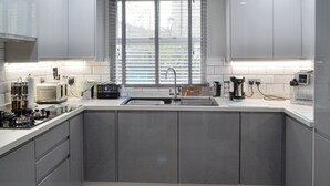 Una cocina moderna con armarios grises, horno empotrado, pileta y una ventana con persianas.