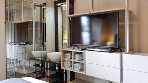 Un baño moderno con un espejo grande, televisión, lavamanos y un perchero para toallas.