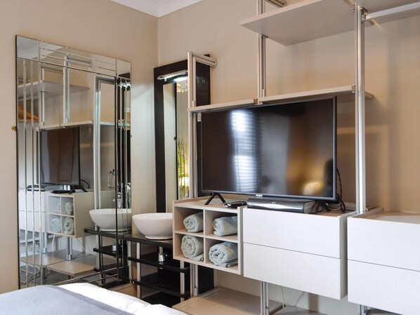 A modern bathroom with a large mirror, a television, a sink, and a towel rack.