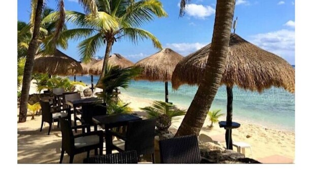 Een restaurant aan het strand met rieten parasols en terrasplaatsen.