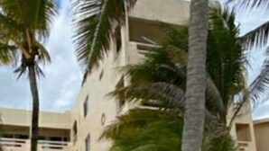 Een strandhotel met meerdere balkons, palmbomen en een zandpad.