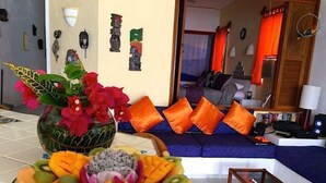 Una sala de estar con un frutero, un sofá con cojines naranja y una mesa de centro.