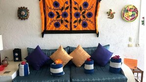 Una habitación con sofá cama, almohadones decorativos, cuadros en la pared y una mesita con un altavoz y un florero.