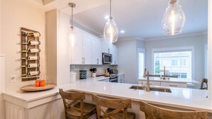Una cocina moderna con armarios blancos, una isla central con taburetes de bar, iluminación colgante y una estantería para vinos en la pared.