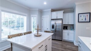 Una cocina moderna con armarios blancos, un refrigerador de acero inoxidable y una isla grande con un centro de madera.