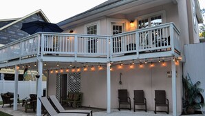 Casa de dos pisos con un patio cubierto que incluye asientos exteriores y luces colgantes.