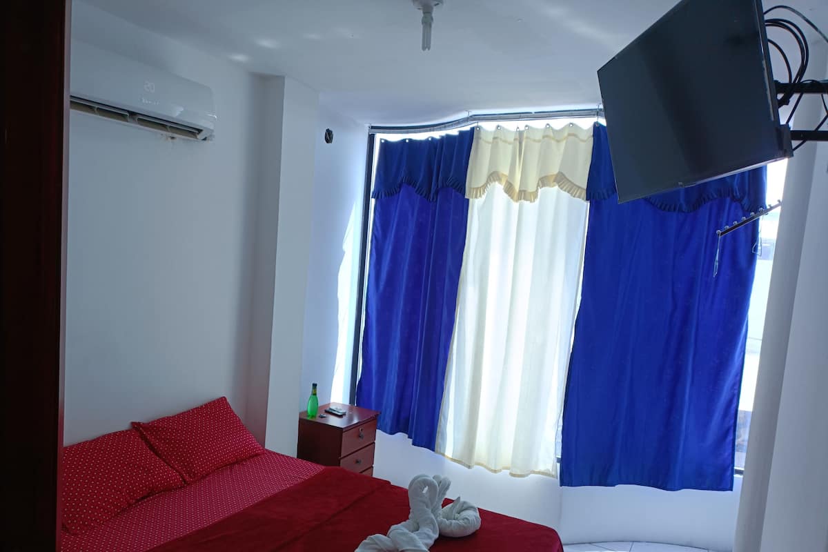 Une chambre d’hôtel avec un lit, une petite table sur laquelle se trouve une bouteille, une télévision et des rideaux.