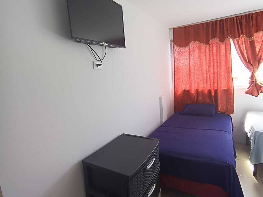 A bedroom with a bed, a TV mounted on the wall, and a small black storage unit.