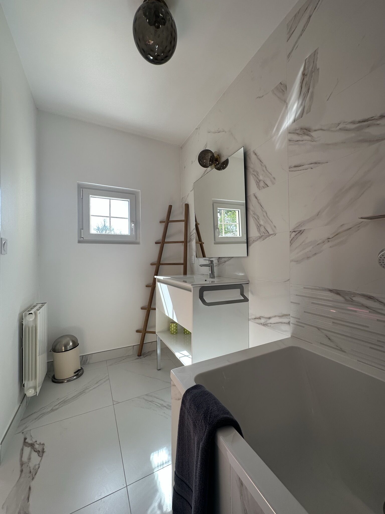 A bathroom with a bathtub, a sink, a mirror, a window, and a radiator.