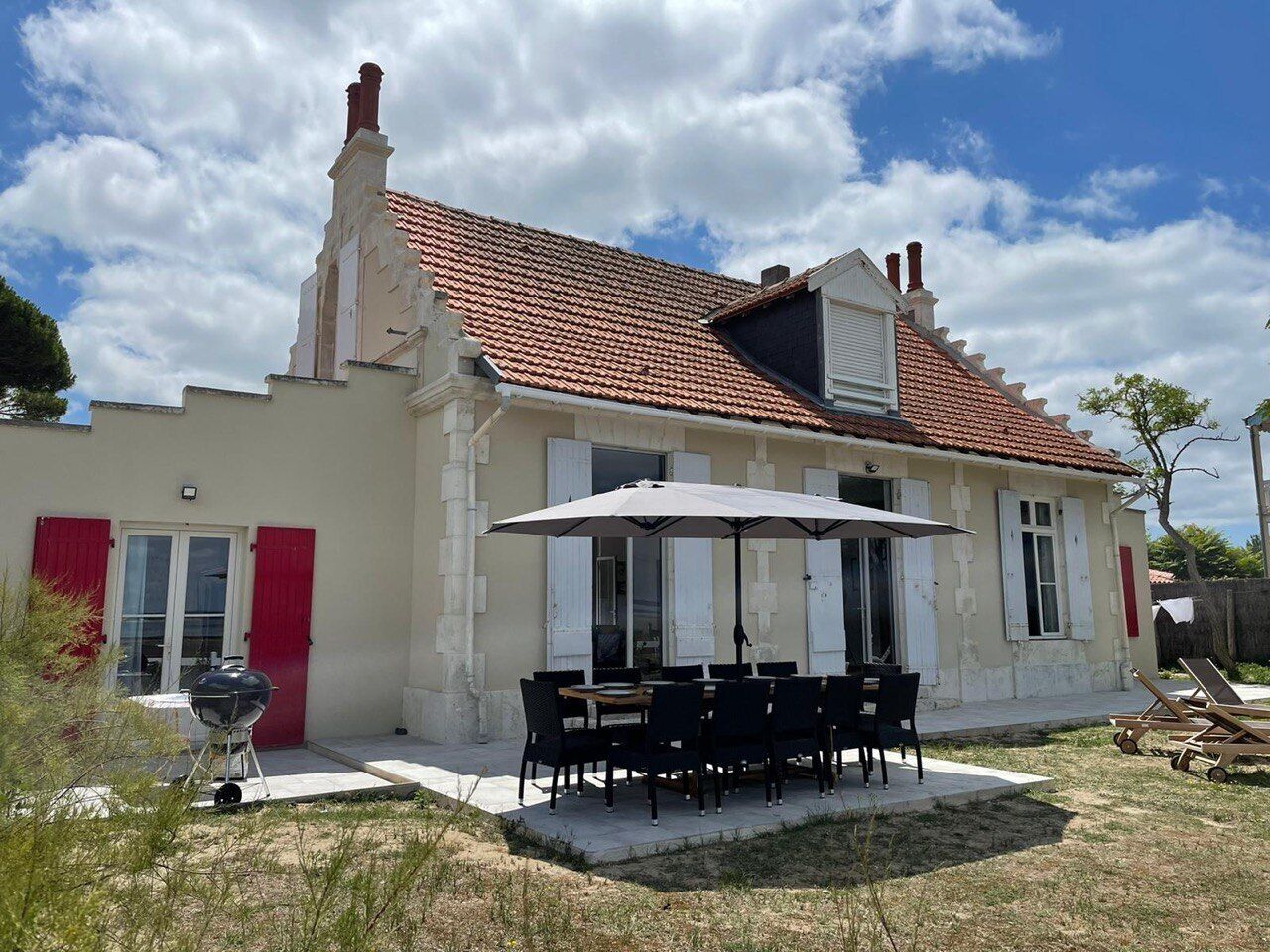 A house with a tiled roof, a patio with a table and chairs, and a barbecue grill.