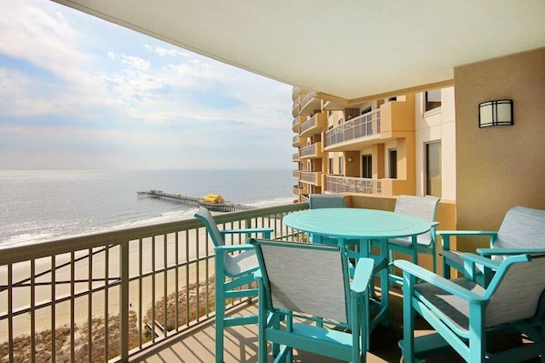 Un balcón con sillas turquesas y una mesa con vistas a una playa y un muelle.