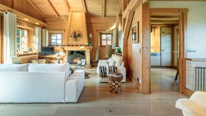 Een ruime woonkamer met een open haard, witte banken en een houten plafond.